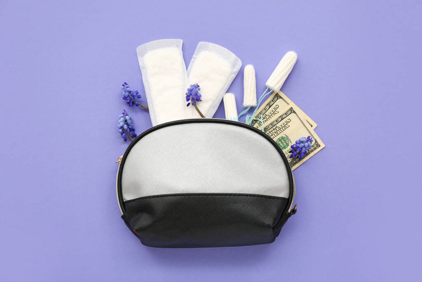 Lady 's cosmetische tas met tampons, menstruatiepads en geld op violette achtergrond - Foto, afbeelding