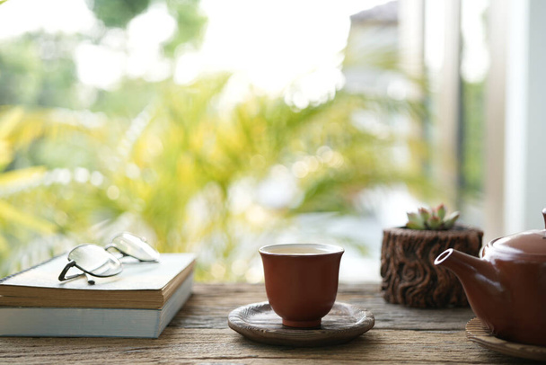 Földi eszközök teáskanna poharak és teáscsésze és notebook és kaktusz edény fából készült asztalon - Fotó, kép