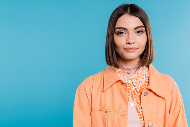 generation z, portrait of pretty woman, young fashion model looking at camera on blue background, orange shirt, short brunette hair, pierced nose, summer outfit, gen z fashion  - Photo, Image