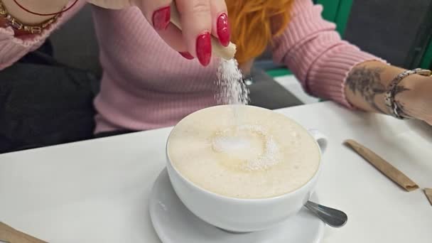 Añadiendo azúcar de una chica a una taza de café con leche de cerámica blanca en un restaurante. Movimiento lento - Metraje, vídeo