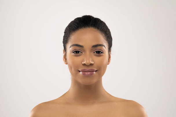 Beautiful millennial african american woman posing half-naked on colorful grey studio background, smiling at camera, showing glowing perfect young skin, closeup, copy space - Photo, image