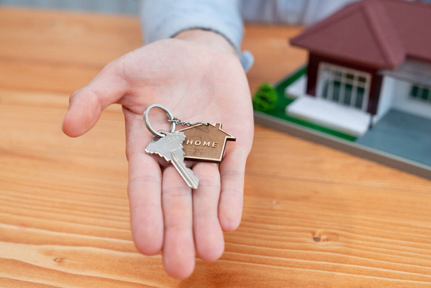 Agente immobiliare presenta la chiave di casa sulla sua mano sopra tavolo di legno circondato da calcolatrice e documenti legali, come un gesto simbolico per la vendita di casa persuasiva e offerta ipotecaria. Entità - Foto, immagini