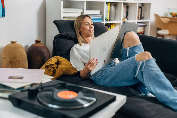 A pretty woman listening to music on gramophone and looking at t the covers of her records. - Fotoğraf, Görsel