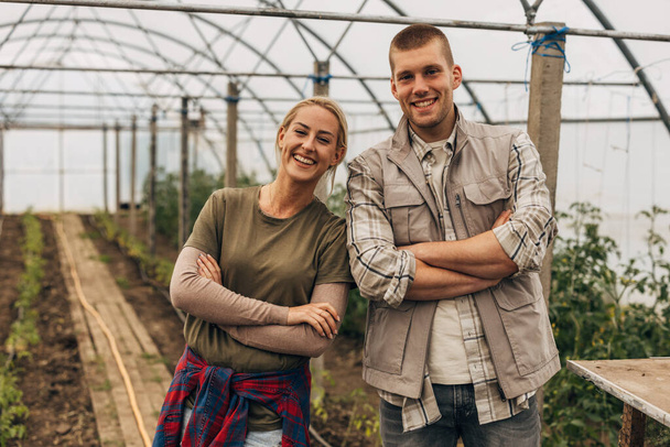 Happy young man and woman standing in the greenhouse together. - Foto, Imagen