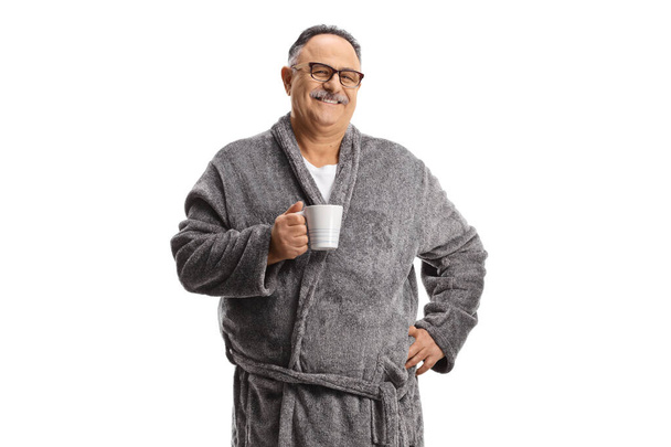 Smiling mature man wearing a grey robe and holding a cup isolated on white background - Photo, image