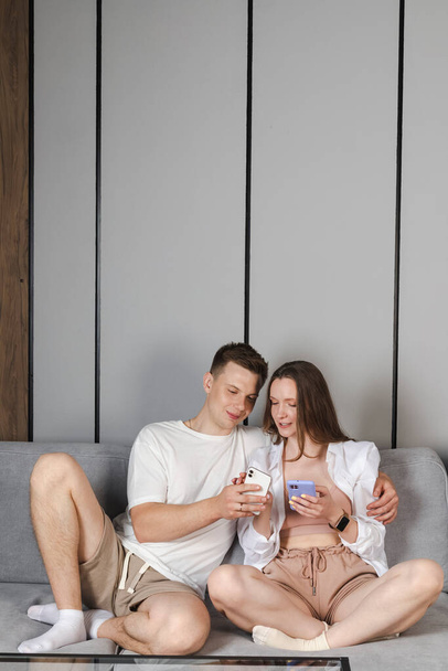 Happy young adult couple family parents together in the living room, looking at the phones, sharing photos, remember happy moments and memories, spending time together. - Fotoğraf, Görsel