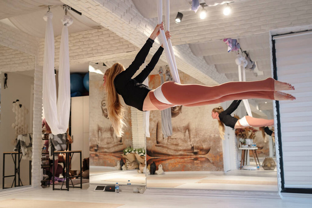 workshop of air yoga and stretching in yoga studio. women practices different inversion antigravity yoga with hammock. balance between mental and physical, one person effort and achievement concept - Photo, image
