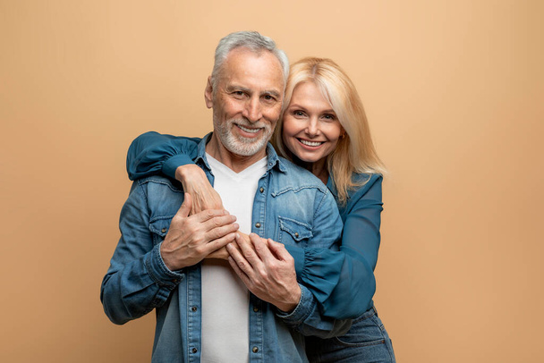 Portrét milující veselý krásný seniorský pár šedovlasý pohledný muž a blond hezká dáma lepící se na barevné pastelové pozadí studia, usmívající se do kamery. Láska, náklonnost, manželství - Fotografie, Obrázek