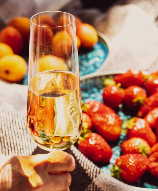 ピクニック中のシャンパンや白ワインのグラスの上にイチゴ。豪華なライフスタイル、旅行のコンセプト。乾杯用に手に入れたグラス。熟した果実。ワインの試飲。ブドウ畑だ。夏の果物。美学 - 写真・画像