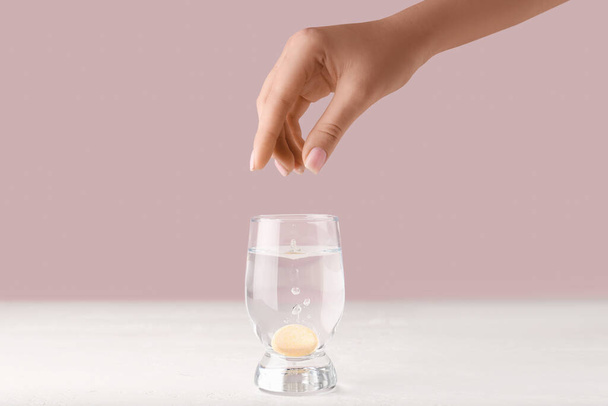 Mujer poniendo tableta soluble en un vaso de agua sobre fondo rosa - Foto, imagen
