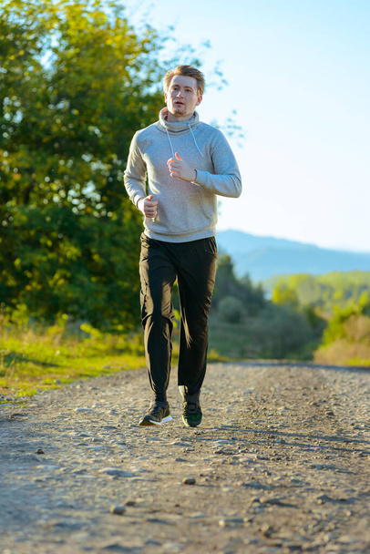 Running man jogging in rural nature at beautiful summer day. Sport fitness model caucasian ethnicity training outdoor. - Photo, image