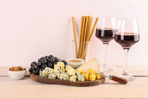 Κομμάτια νόστιμου τυριού, σταφυλιών και ποτηριών με κρασί στο τραπέζι - Φωτογραφία, εικόνα