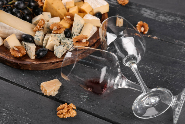 Тарелка с кусочками вкусного сыра и бокалами вина на темном деревянном фоне - Фото, изображение