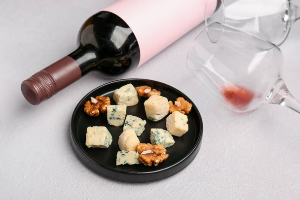 Pieces of tasty cheese, glasses and bottle with wine on light background - Photo, Image