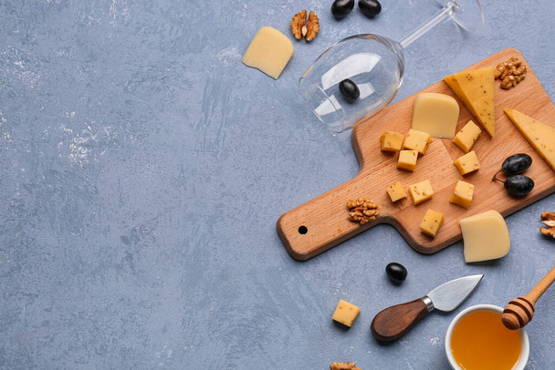 Tablero de madera con trozos de sabroso queso, copa de vino y miel sobre fondo gris - Foto, imagen