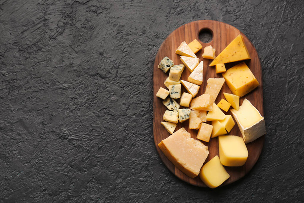 Board with pieces of tasty cheese on dark background - 写真・画像