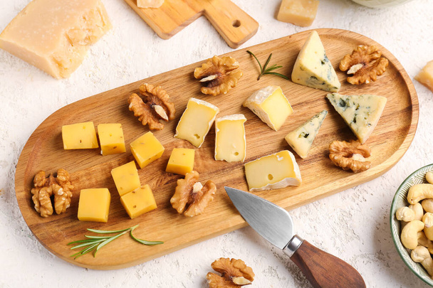 Wooden board with pieces of tasty cheese on light background - Zdjęcie, obraz