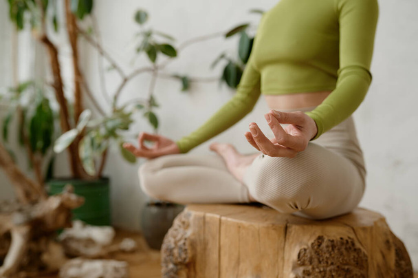 Здоровая женщина практикует медитацию и упражнения йоги релаксации в помещении. Спортсменка делает Ардха Падмасану жест мудры для достижения гармонии чакр. Снимок с урожая - Фото, изображение