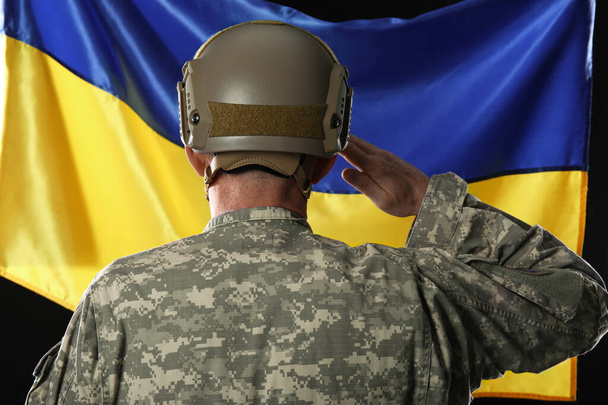 Reifer Soldat salutiert gegen Flagge der Ukraine, Rückseite - Foto, Bild