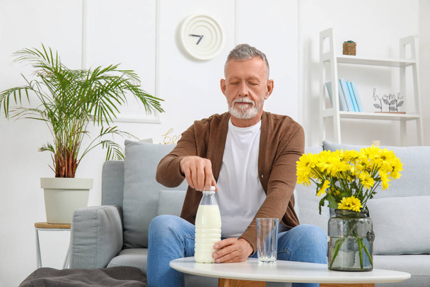 Hombre maduro abriendo botella de leche en casa - Foto, imagen