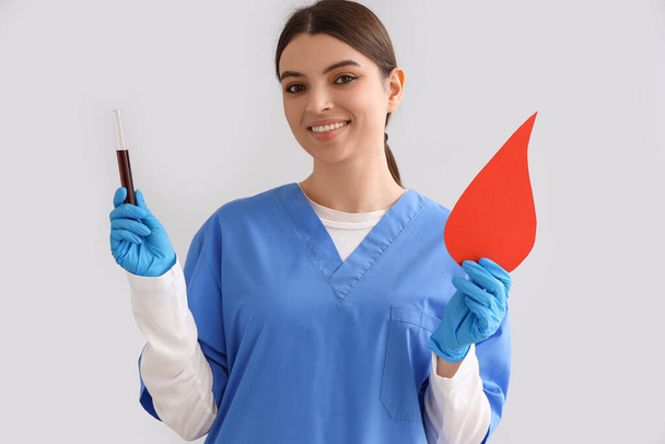 Female nurse with test tube and paper blood drop on light background - Photo, Image
