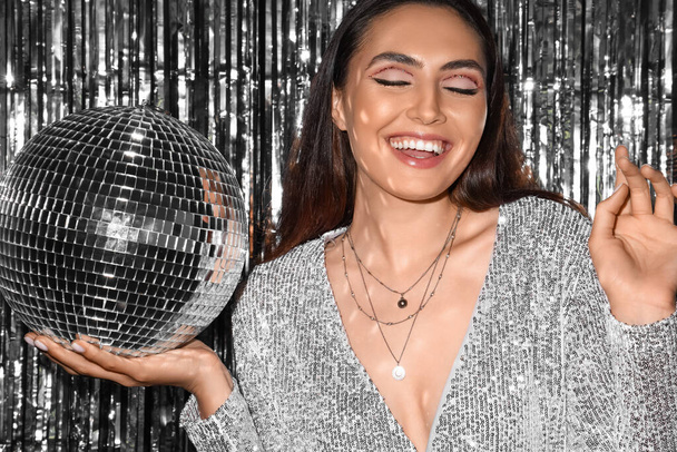 Donna alla moda sorridente in abito scintillante con palla da discoteca contro fili d'argento - Foto, immagini