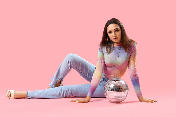 Fashionable beautiful young woman with disco ball sitting on pink background - Photo, Image