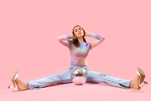 Modieuze mooie jonge vrouw met discobal zittend op roze achtergrond - Foto, afbeelding