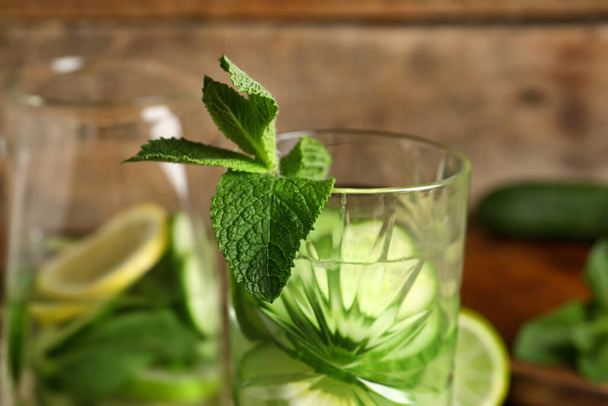 Glass and jug of infused water with cucumber slices on wooden background - Valokuva, kuva