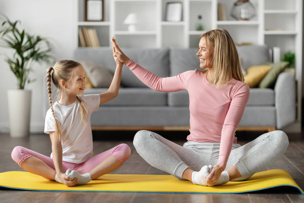 Boldog anya és nő gyermek ajándékozás pacsi közben edzés együtt otthon, vidám fiatal anya és kicsi lánya gyakorló sport, csinál pillangó nyújtás gyakorlat a nappaliban belső - Fotó, kép
