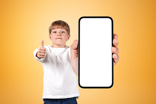 Young student wearing casual wear is holding smartphone case with copy space standing in front of orange wall in background. Concept of mobile application and social media, progressive kids - Valokuva, kuva