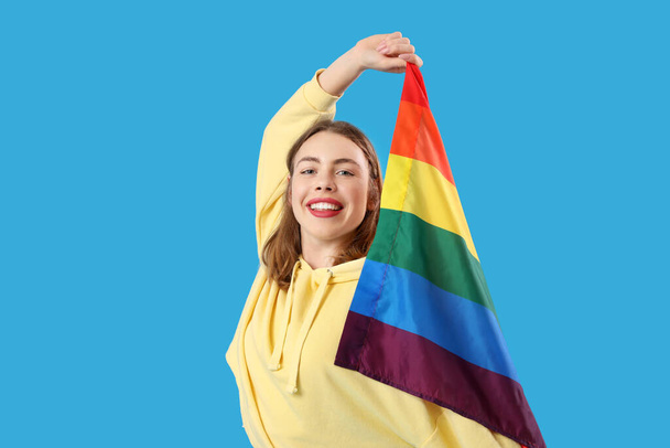 Mujer joven feliz con bandera LGBT sobre fondo azul - Foto, Imagen