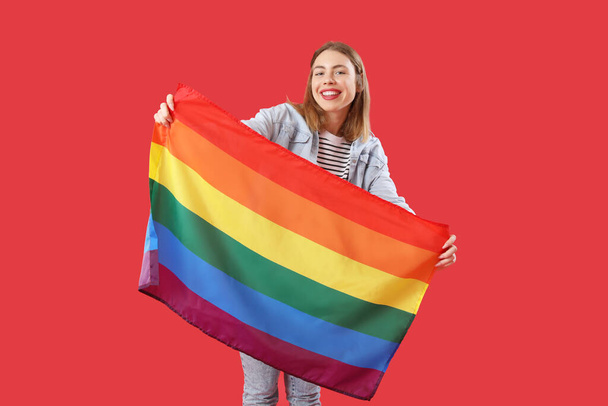 Kırmızı arka planda LGBT bayrağı olan genç bir kadın. - Fotoğraf, Görsel