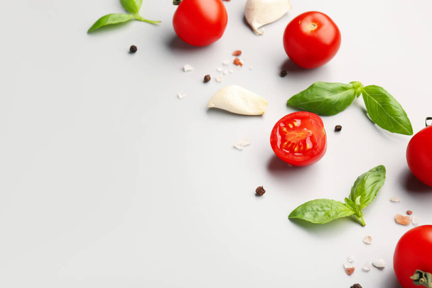 Composición con tomates cherry maduros, hojas de albahaca, ajo y pimienta sobre fondo claro, primer plano - Foto, imagen