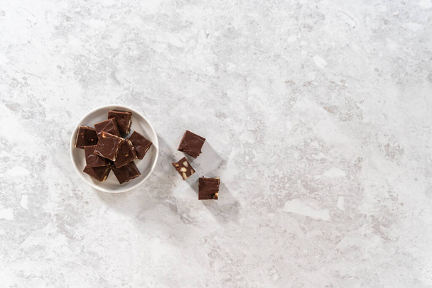 Flach lag er. Hausgemachte Schokolade Macadamia Fudge quadratische Stücke auf einem weißen Teller. - Foto, Bild