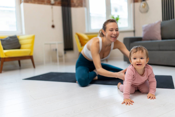 Healthy development. Athletic mother and baby girl exercising together at home playing in living room. - Foto, imagen