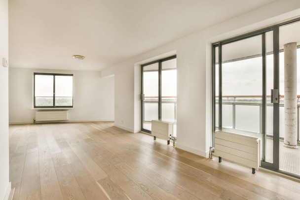 prázdný obývací pokoj s dřevěnou podlahou a posuvnými skleněnými dveřmi, které se otevírají na balkon s výhledem na vodu - Fotografie, Obrázek