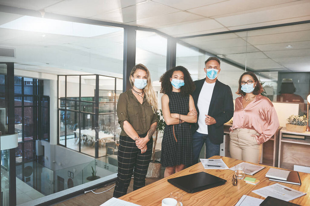 Covid nem fog az üzleti terveink útjába állni. egy változatos csoport üzletember, akik együtt állnak az irodában és maszkot viselnek. - Fotó, kép