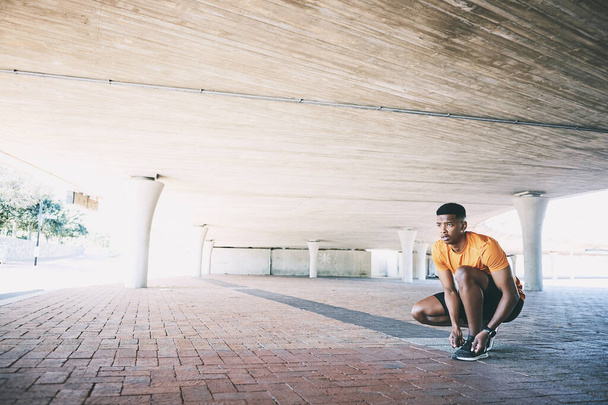 Getting fit takes mental muscle too. a young man tying his shoelaces during a workout against an urban background - Photo, Image