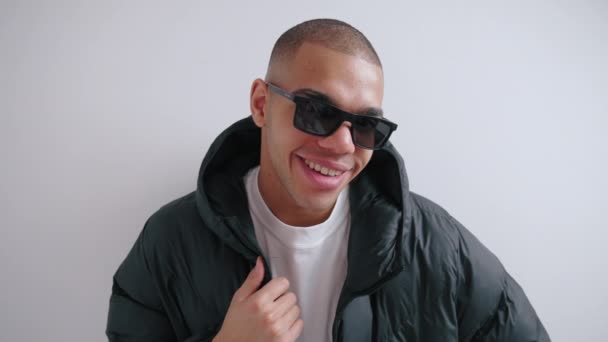 African American man in sunglasses and a puffer jacket smiling at the camera isolated against a white background. High quality 4k footage - Footage, Video