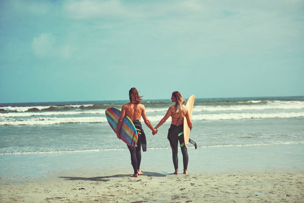 Наше кохання зробить це крізь суворі води. молода пара, що йде на пляжі з дошками для серфінгу
 - Фото, зображення