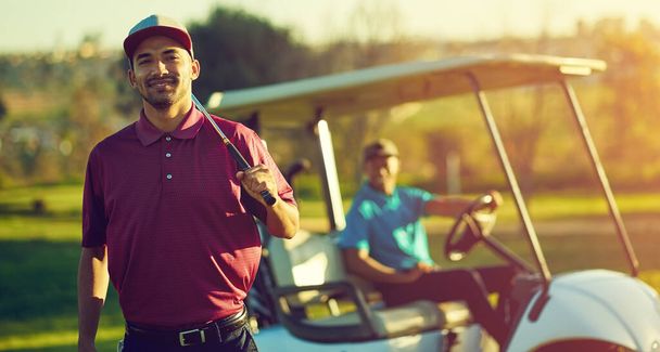 Golf je hra gentlemanů. Portrét golfisty držícího hůl s kočárkem rozmazaným v pozadí - Fotografie, Obrázek