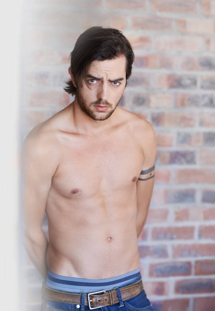 Expressing my masculinity. Portrait of brooding attractive male with his shirt off standing against a brick wall - Photo, Image