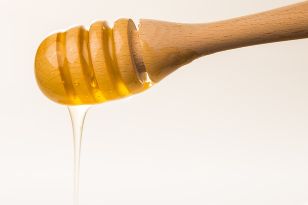 Honey dripping from a wooden honey dipper isolated on white back - Fotoğraf, Görsel
