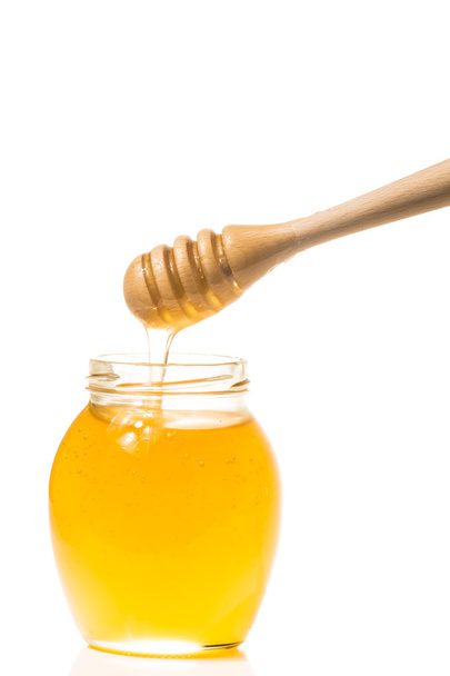 Jar of honey with wooden drizzler isolated on white background - Fotoğraf, Görsel