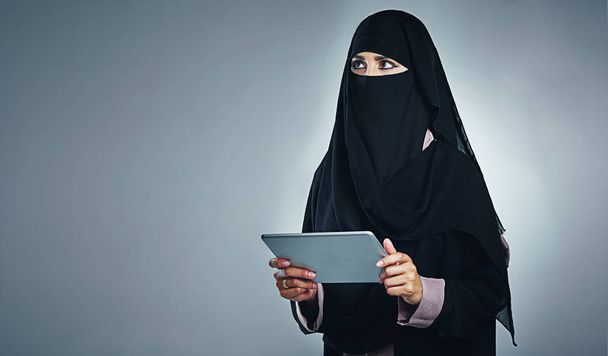 Las vidas mucho más fácil en la edad de la aplicación. Foto de estudio de una mujer joven con una burka y una tableta digital sobre un fondo gris - Foto, Imagen