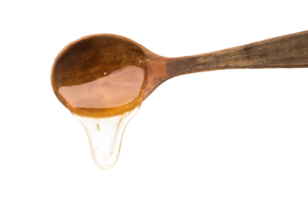 Honey dripping from a wooden honey dipper isolated on white back - Foto, afbeelding
