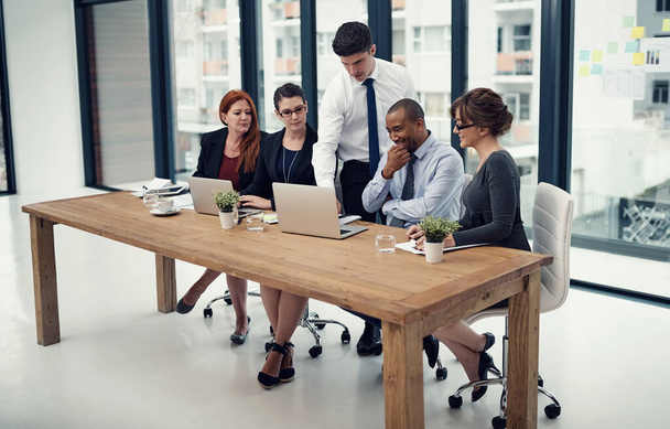Их бизнес-процессы просто не завершены без технологий. группа бизнесменов, использующих ноутбук вместе во время встречи в офисе - Фото, изображение