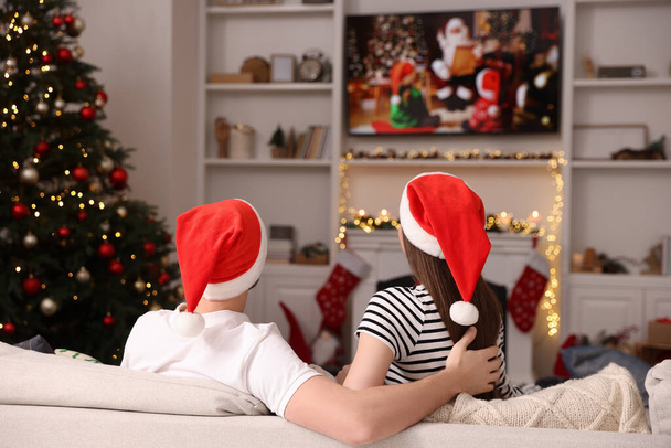居心地の良い部屋でテレビを通してクリスマス映画を見ているカップル、バックビュー。冬の休日の雰囲気 - 写真・画像