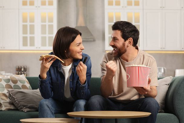 Happy couple watching TV with popcorn and pizza on sofa at home - Foto, Imagem